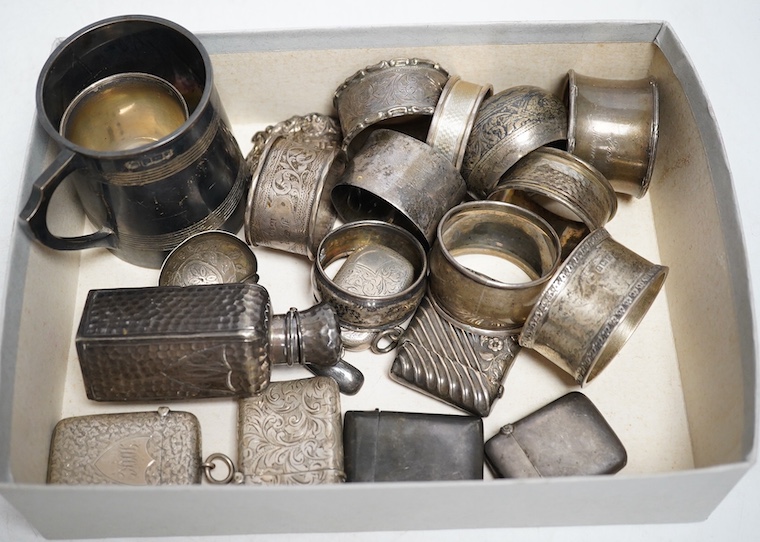 A group of small silver to include a christening mug, 143g, an egg cup, ten various napkin rings, 184g, a spot hammered bottle, a sherry label, six vesta cases, 152g and a caddy spoon. Condition - fair